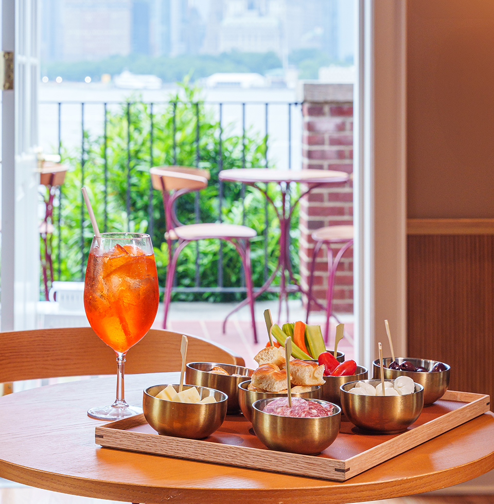 Elegant table setting with assorted appetizers and a cocktail, overlooking a city skyline through a large window.